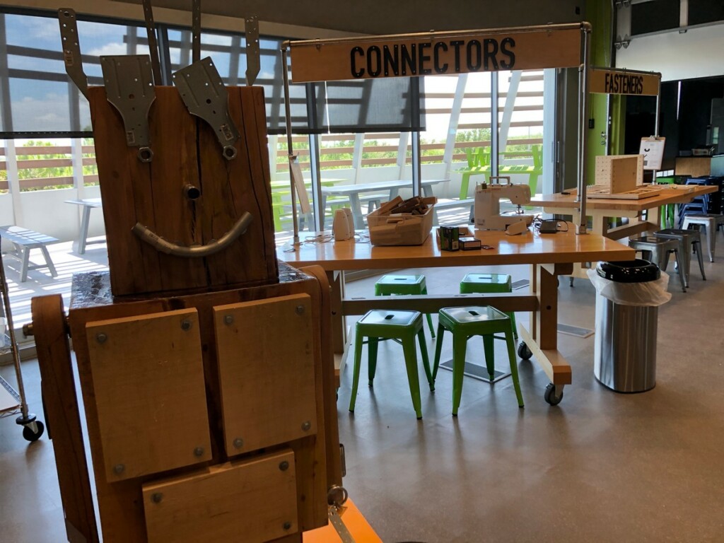 a collaborative art sculpture where visitors can attach features to a wooden robot with magnets or practice using a drill or wrench.